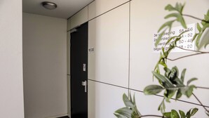 Un pasillo con una puerta marcada con los números 18-20, un letrero de prohibido fumar y una planta en primer plano.