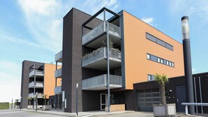 Un edificio moderno de varios pisos con balcones, un garaje y un muro de piedra.