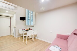 Uma sala de estar moderna com um sofá rosa, uma área de jantar com mesa e cadeiras, uma máquina de lavar roupa e uma TV na parede.