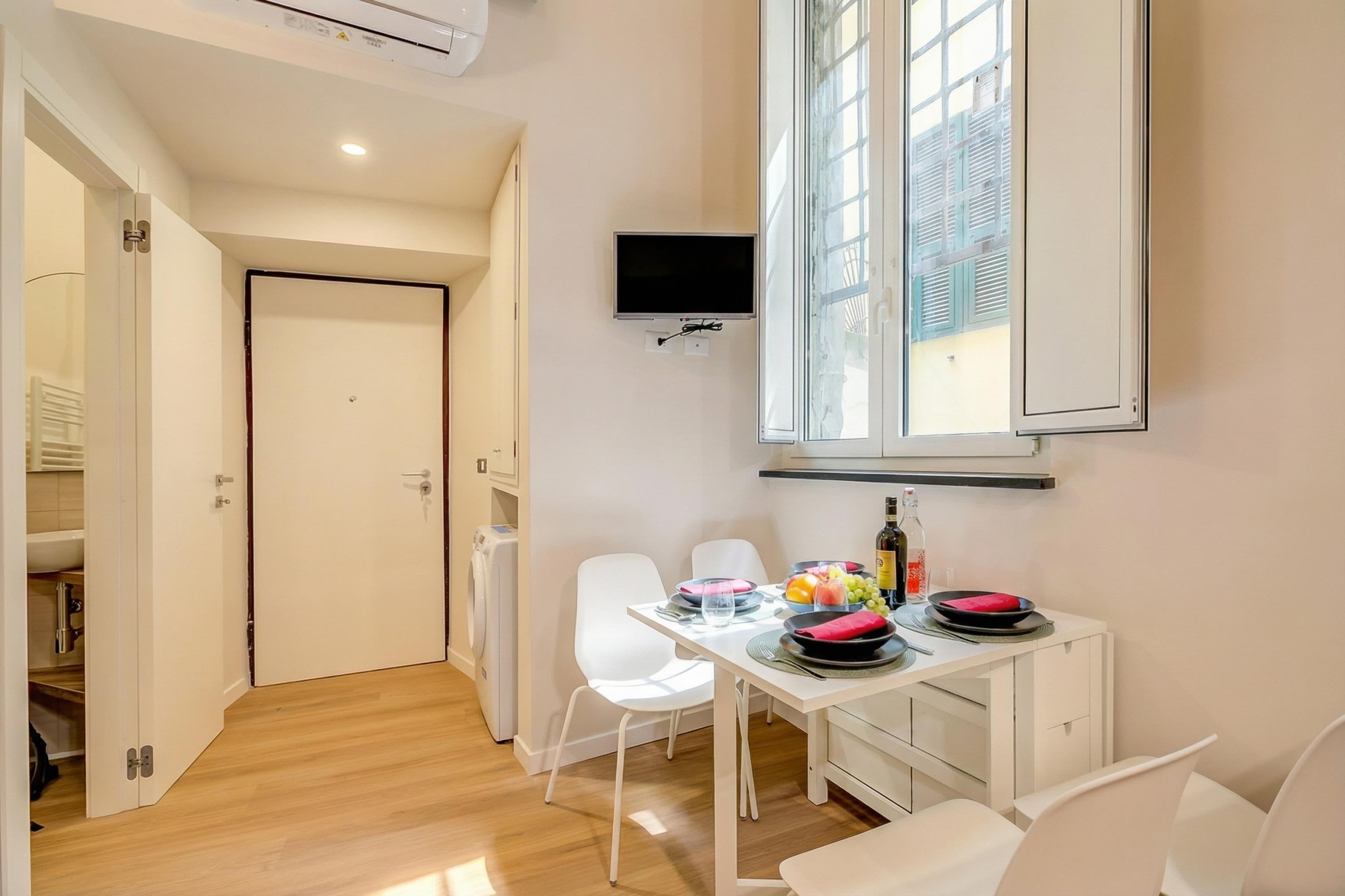 Una cucina moderna con zona pranzo, una TV montata sopra il bancone e una finestra che garantisce luce naturale.