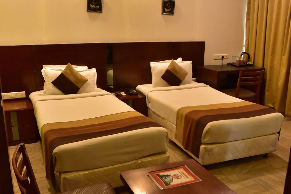 A hotel room with two beds, a desk, a chair, and a table.