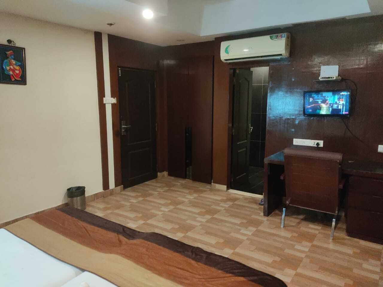 A room with a wooden floor, a bed, a desk, an air conditioner, and a television on the wall.