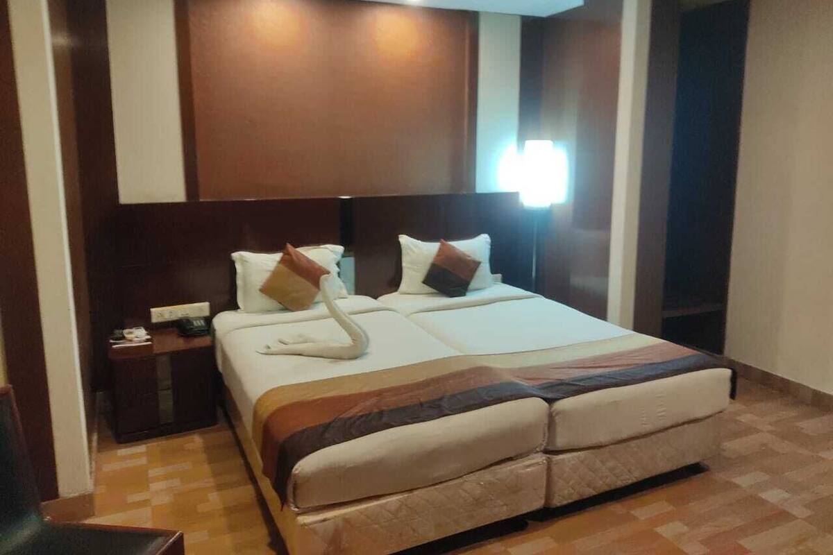 A hotel room with a large bed, a nightstand, and a wall-mounted lamp.