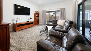 Ein Wohnzimmer mit einem Ledersofa, einem Flachbildfernseher, einer Holzunterhaltungsecke und einem Bücherregal.