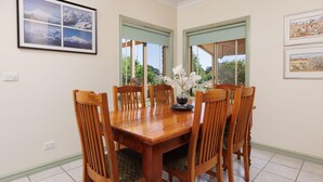A dining room with a wooden table and chairs, framed pictures on the walls, and a window with a view of greenery.