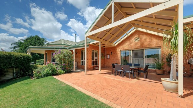 A covered patio with a brick house, outdoor furniture, and a lawn.
