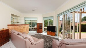 A spacious living room with a brick accent wall, a large sliding glass door leading to a patio, a flat-screen TV on a wooden stand, and a cozy seating area with a patterned rug.