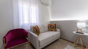 A modern room with a sofa, a red chair, a small table with a lamp, and a window with sheer curtains. - URBAN ROOMS B&R (Málaga)