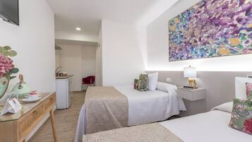 Een hotelkamer met twee bedden, een bureau met telefoon en notitieboekje, een kleine kitchenette en een groot abstract schilderij aan de muur.