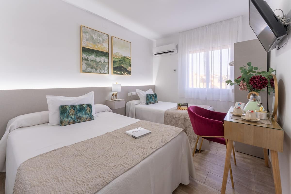 Ett hotellrum med två sängar, ett skrivbord, en stol, en spegel och konstverk på väggen.
