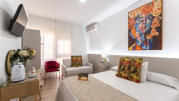 A hotel room with a bed, a desk with a kettle, a chair, a TV, and a painting on the wall. - URBAN ROOMS B&R (Málaga)