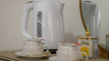 Una tetera eléctrica blanca con temporizador digital, dos tazas blancas sobre platillos y un pequeño recipiente con tapa dorada.