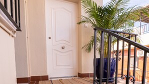 A staircase leading to a white door, with a potted plant on the right and a metal railing. - URBAN ROOMS B&R (Málaga)