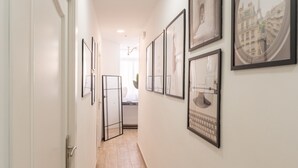 A hallway with framed pictures on the walls, a door on the left, and a tiled floor. - URBAN ROOMS B&R (Málaga)