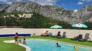 Ein Swimmingpool mit Liegestühlen und Sonnenschirmen, vor einer Bergkulisse.