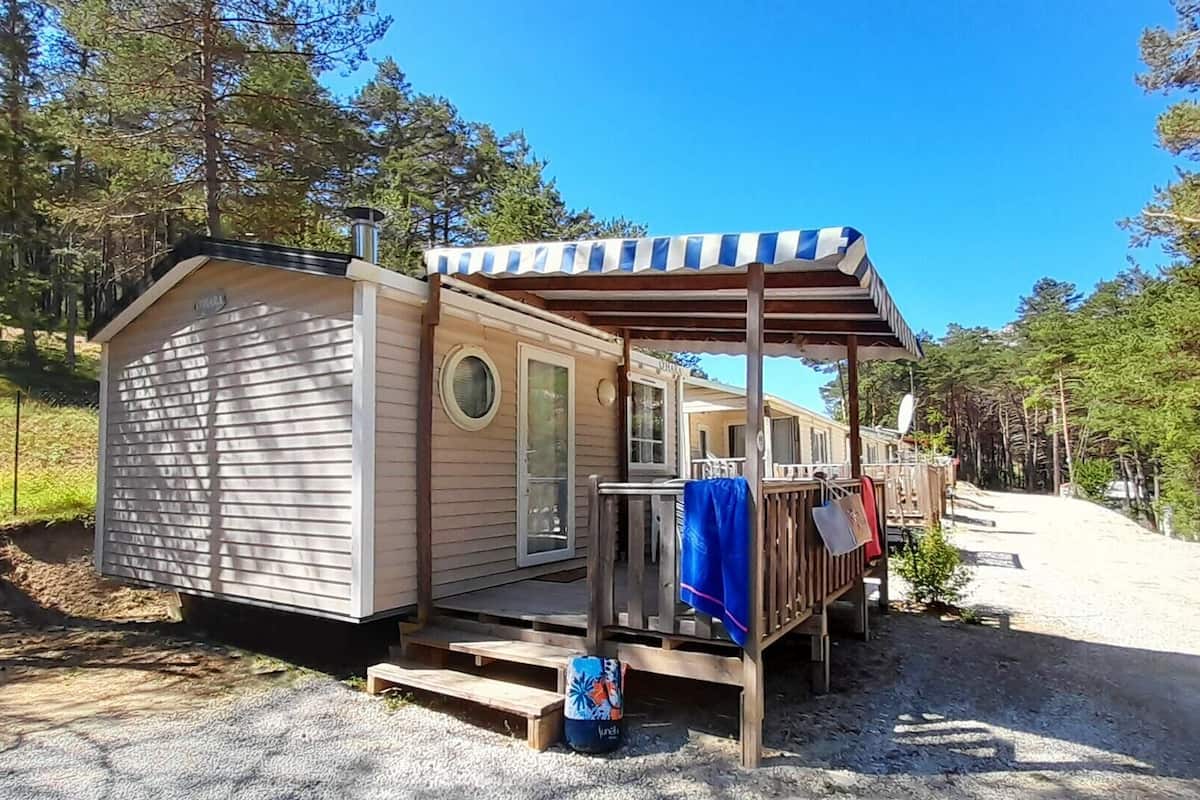 A small cabin with a porch, a covered deck, and a gravel driveway.
