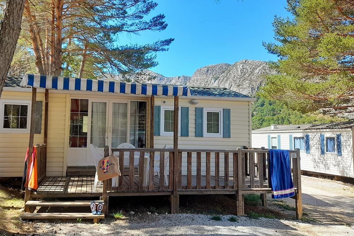 A small, single-story cabin with a porch, a covered deck, and a view of a mountainous landscape.