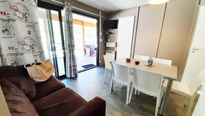 Ein kompakter Wohnbereich mit einer Couch, einem Esstisch mit Stühlen, einer Küchenzeile und einer Glastür zum Außenbereich.