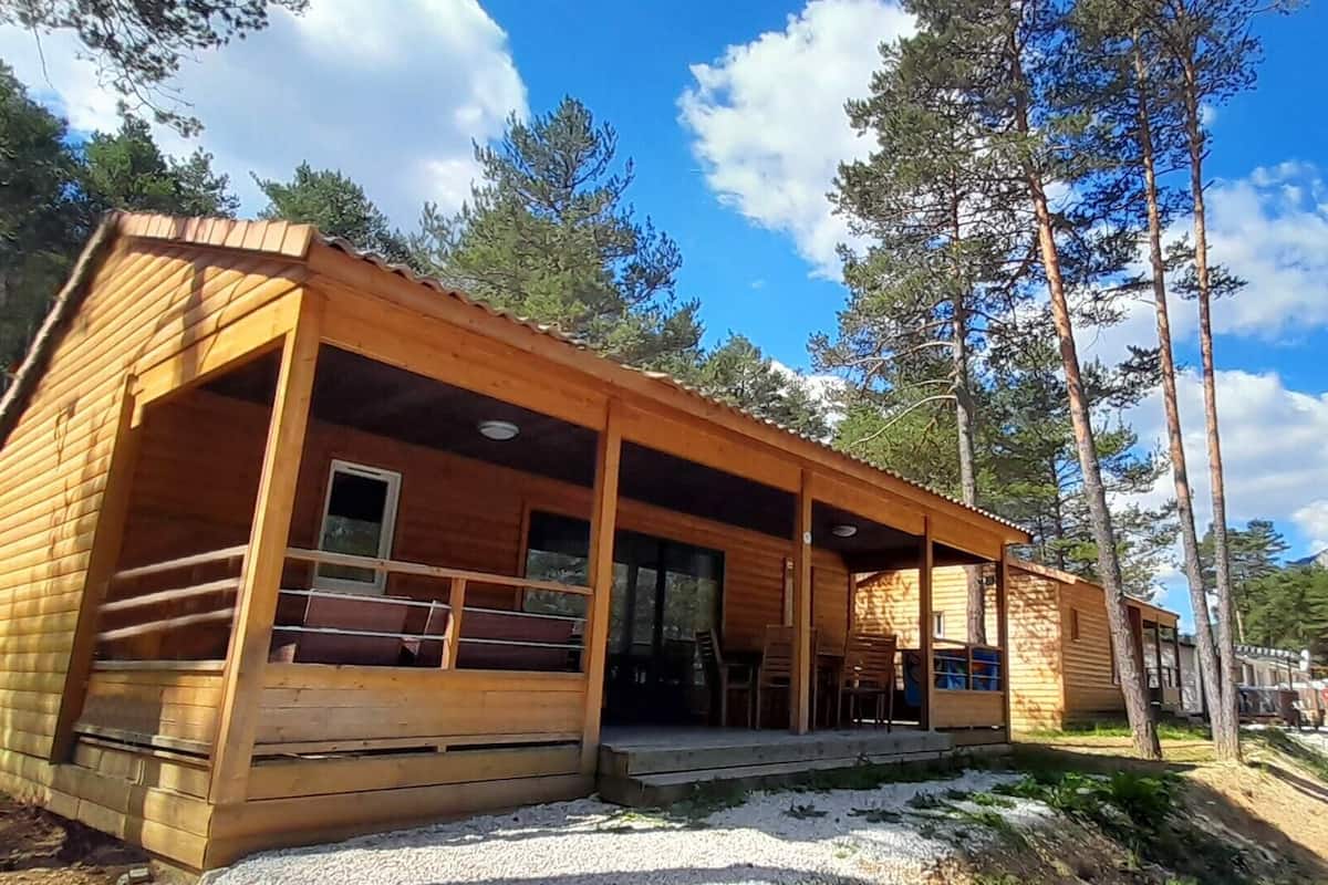 A wooden cabin with a porch, surrounded by trees and a clear sky.