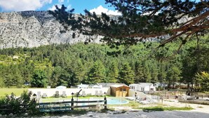 Ein Campingplatz mit Blockhütten, einem Schwimmbad und einer Bergkulisse.