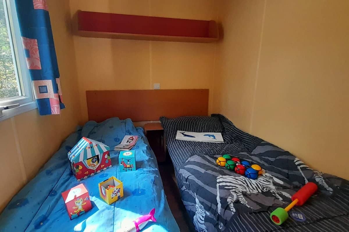 A small, cozy room with two beds, a window with curtains, and various children's toys on the beds.