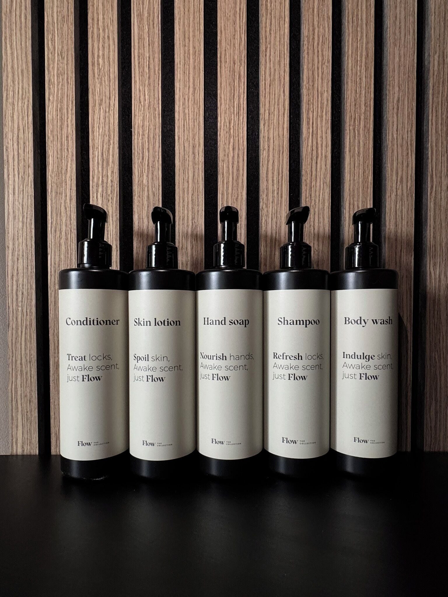 Cinco botellas de productos para el cuidado de la piel con la etiqueta 'Flow' sobre un fondo de madera.
