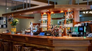 Un espace bar doté d’un comptoir en bois, de tabourets de bar, d’une variété de bouteilles et de verres, ainsi que d’un terminal de paiement numérique.