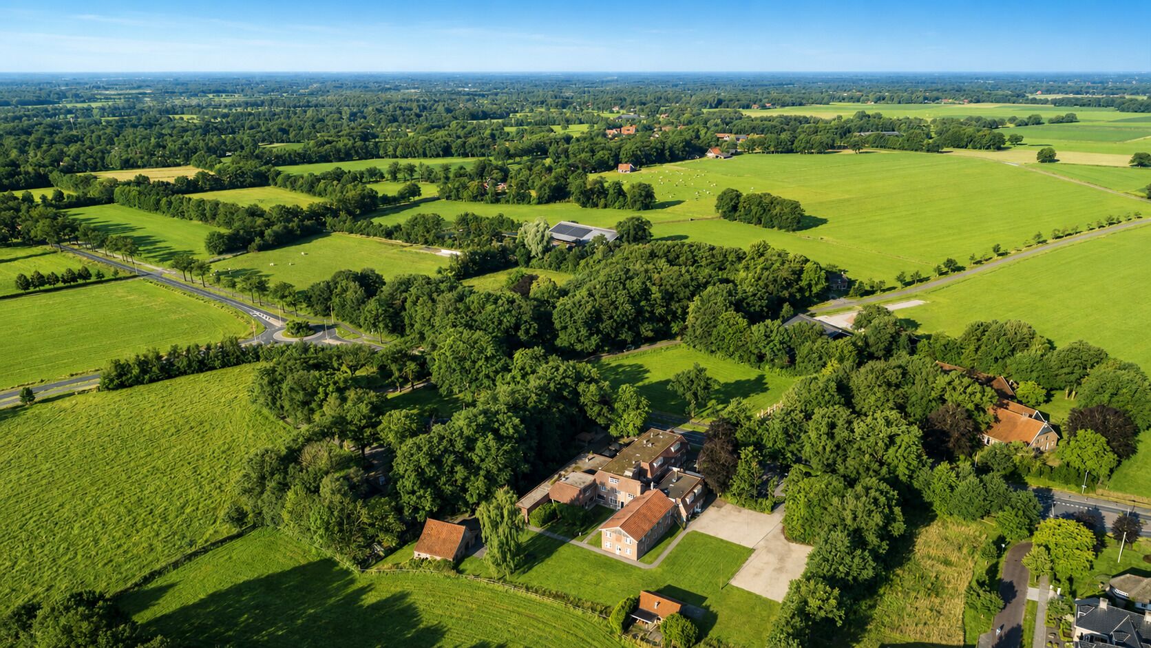 An aerial view of a rural property with multiple buildings, green fields, and a clear sky.