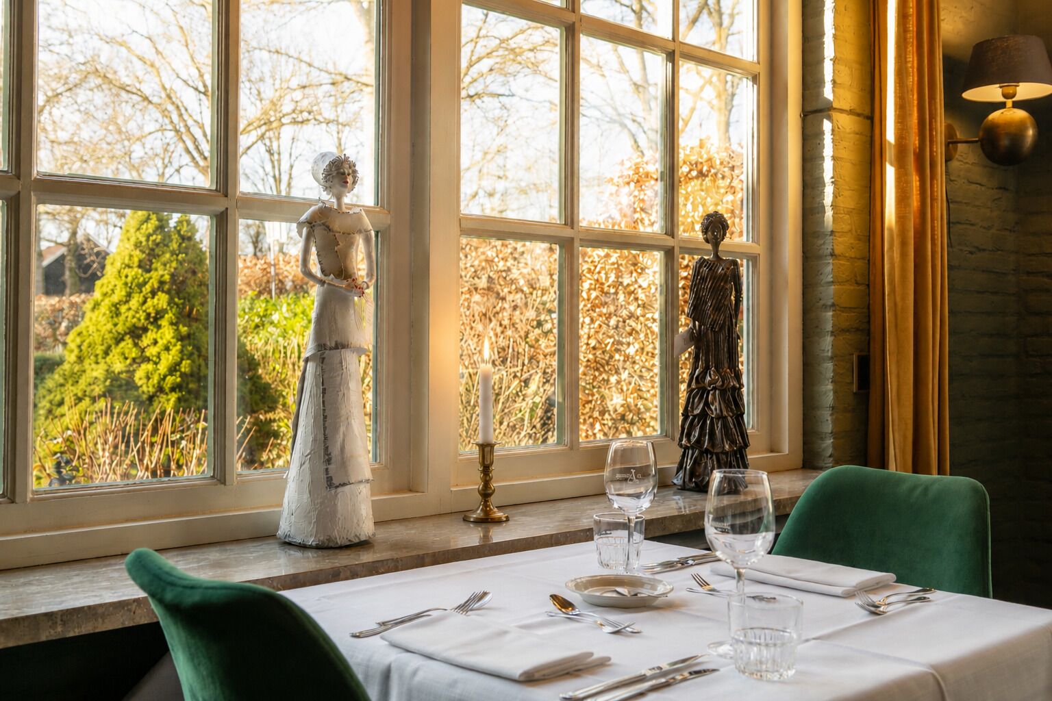 Ein Essbereich mit Tisch für zwei Personen, zwei Stühlen, einem Fenster mit Blick auf Bäume und einer Statue auf der Fensterbank.
