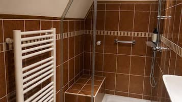 Eine Dusche mit Glasabtrennung, eine weiße Badewanne und ein Handtuchhalter.