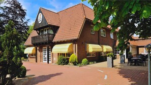 Un bâtiment traditionnel en briques, doté d’un imposant clocher, d’un espace extérieur couvert aménagé en coin salon et d’une cour pavée.