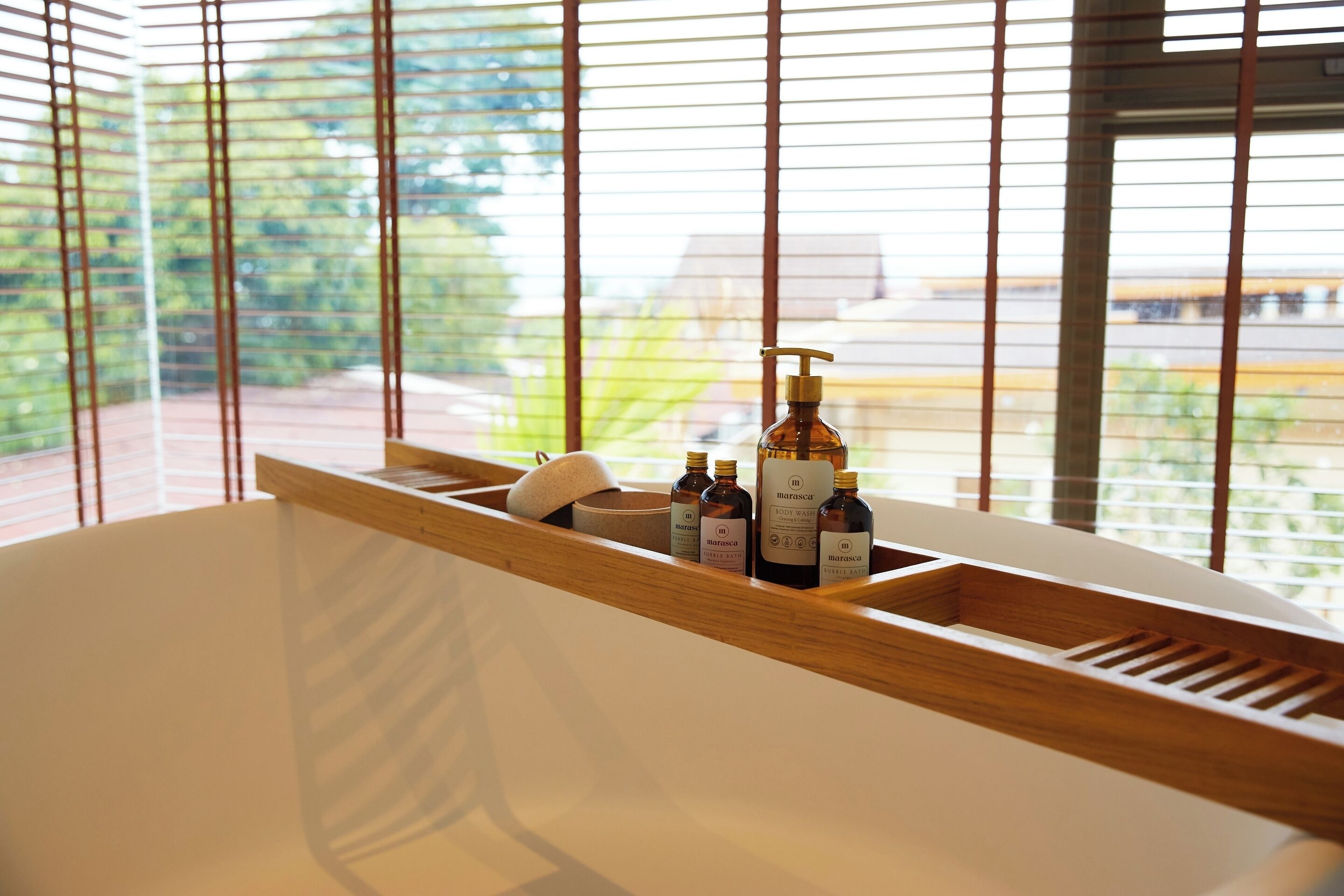 A modern bathroom with a wooden vanity, a bathtub, and a window with blinds.