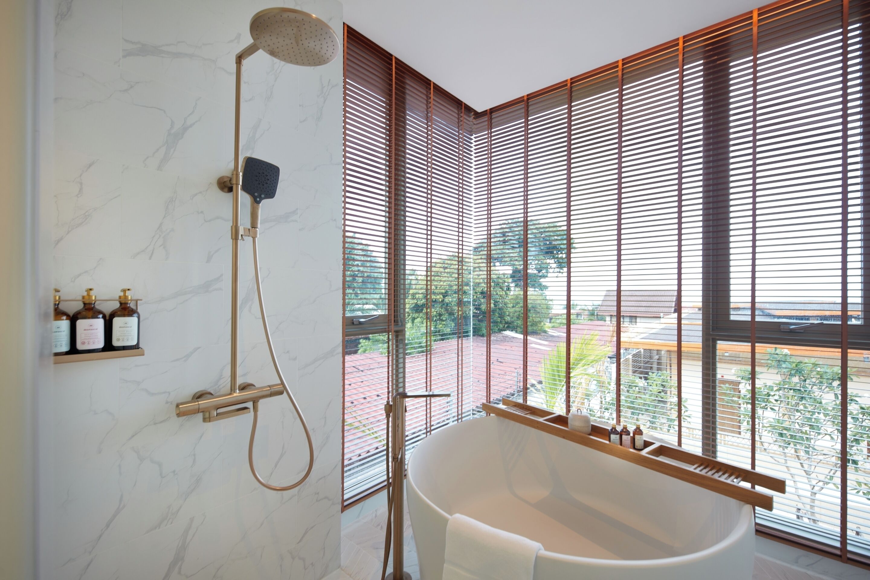 A modern bathroom with a freestanding bathtub, a handheld showerhead, and a large window with blinds.