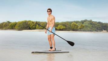 A person paddleboarding on a calm body of water with a forested shoreline in the background.