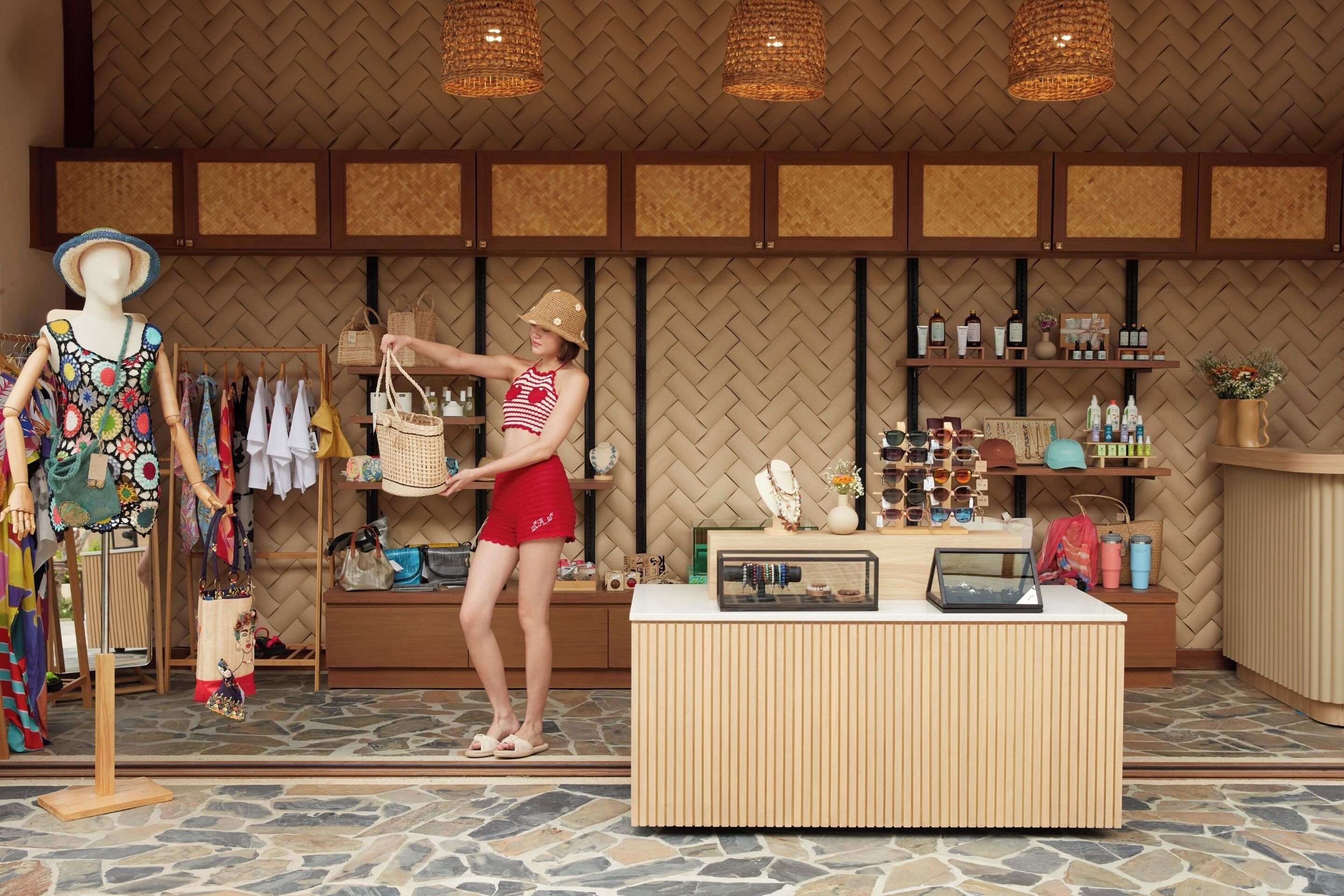 A boutique store with a mannequin displaying colorful dresses, a woman in red shorts and a straw hat browsing items, and a counter with various products.