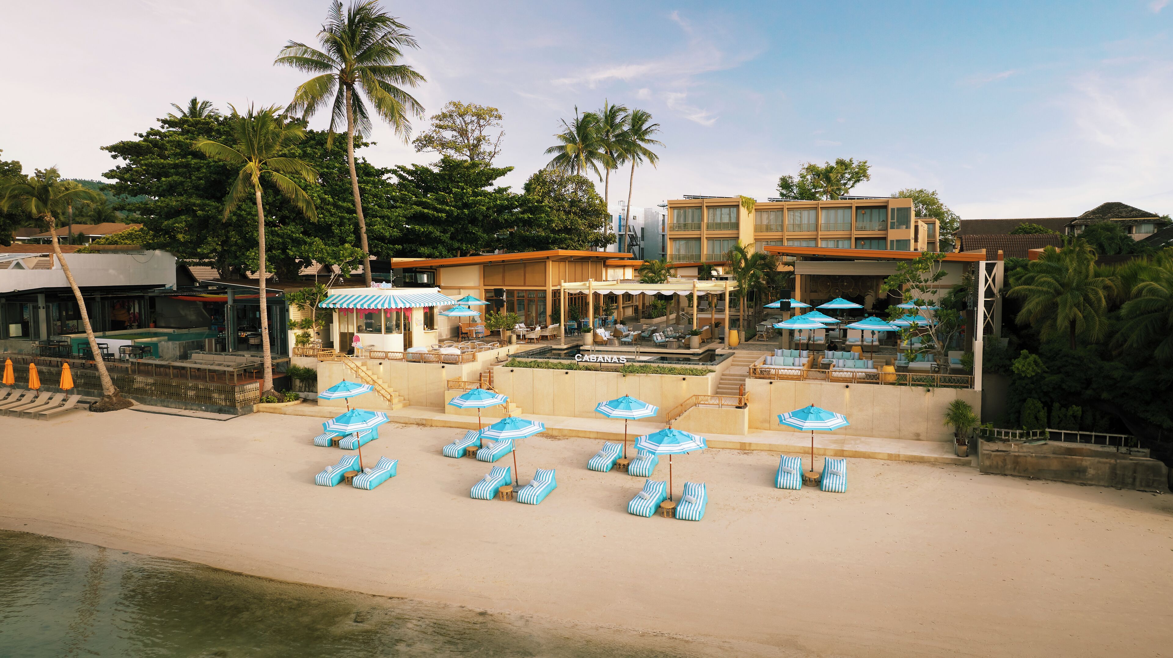 A beachfront hotel with a pool area, sun loungers, and umbrellas.