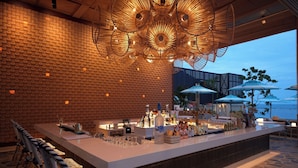 A bar area with a brick wall, a large ceiling light fixture, and outdoor seating with umbrellas. - Marasca Samui - Small Luxury Hotels of the World (Koh Samui)
