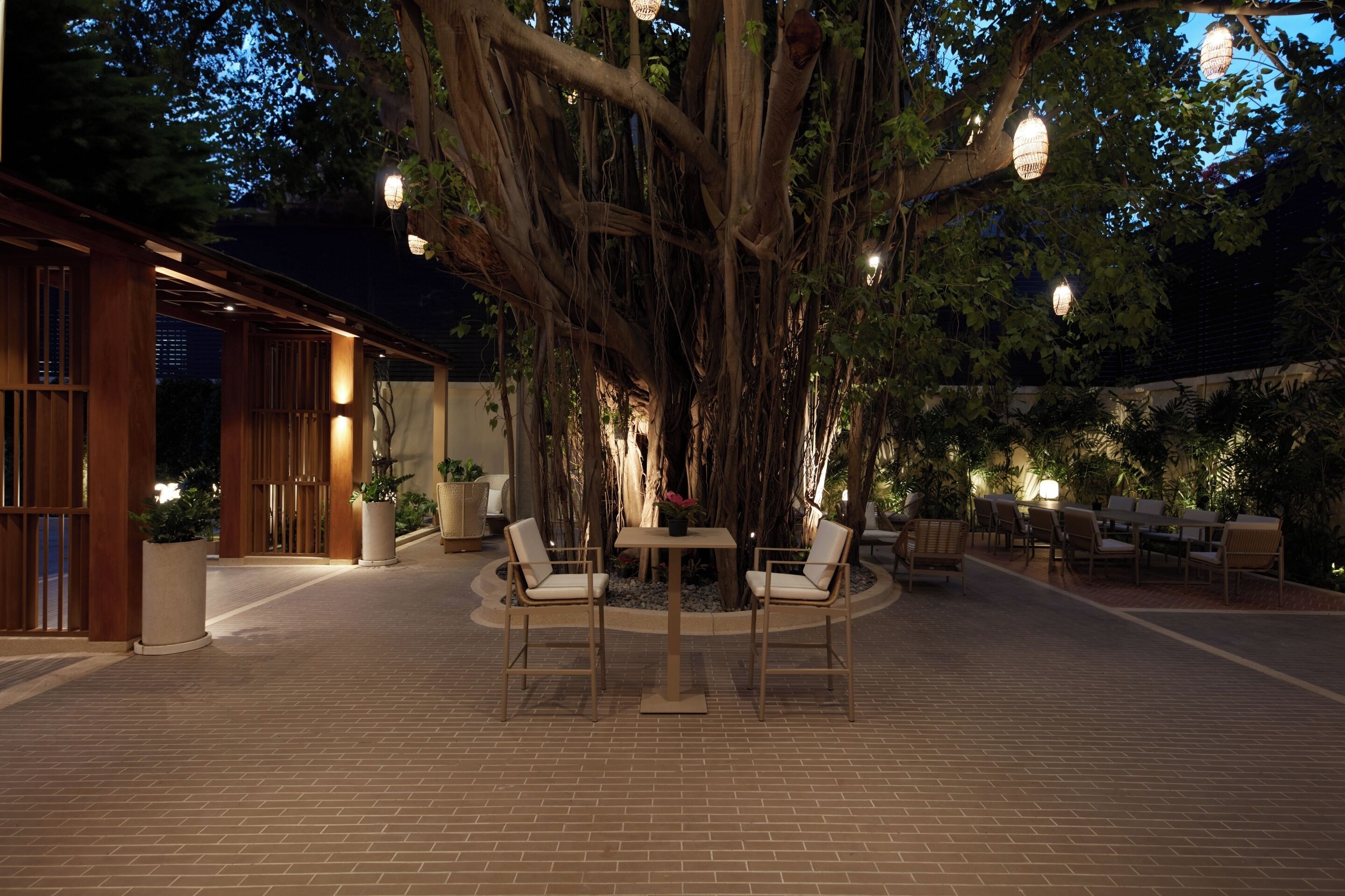 An outdoor patio area with a round table and chairs, surrounded by brick flooring and potted plants.