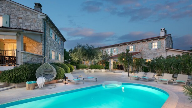 A poolside area with lounge chairs, a stone building, and a clear blue pool.