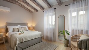 A bedroom with a bed, bedside lamps, a large mirror, a potted plant, and a wicker chair.
