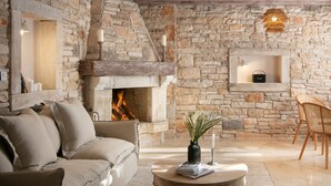 A stone fireplace with a fire, a sofa, a coffee table with books and a vase, and wicker chairs.