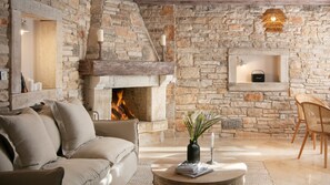 A stone fireplace with a fire, a sofa, a coffee table with books and a vase, and wicker chairs. - Villa Comfort Residence d´Istria by Villas Guide (Kanfanar)