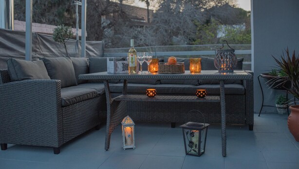 Un espace extérieur aménagé avec un canapé en osier, une table décorée de bougies, de verres et une bouteille.