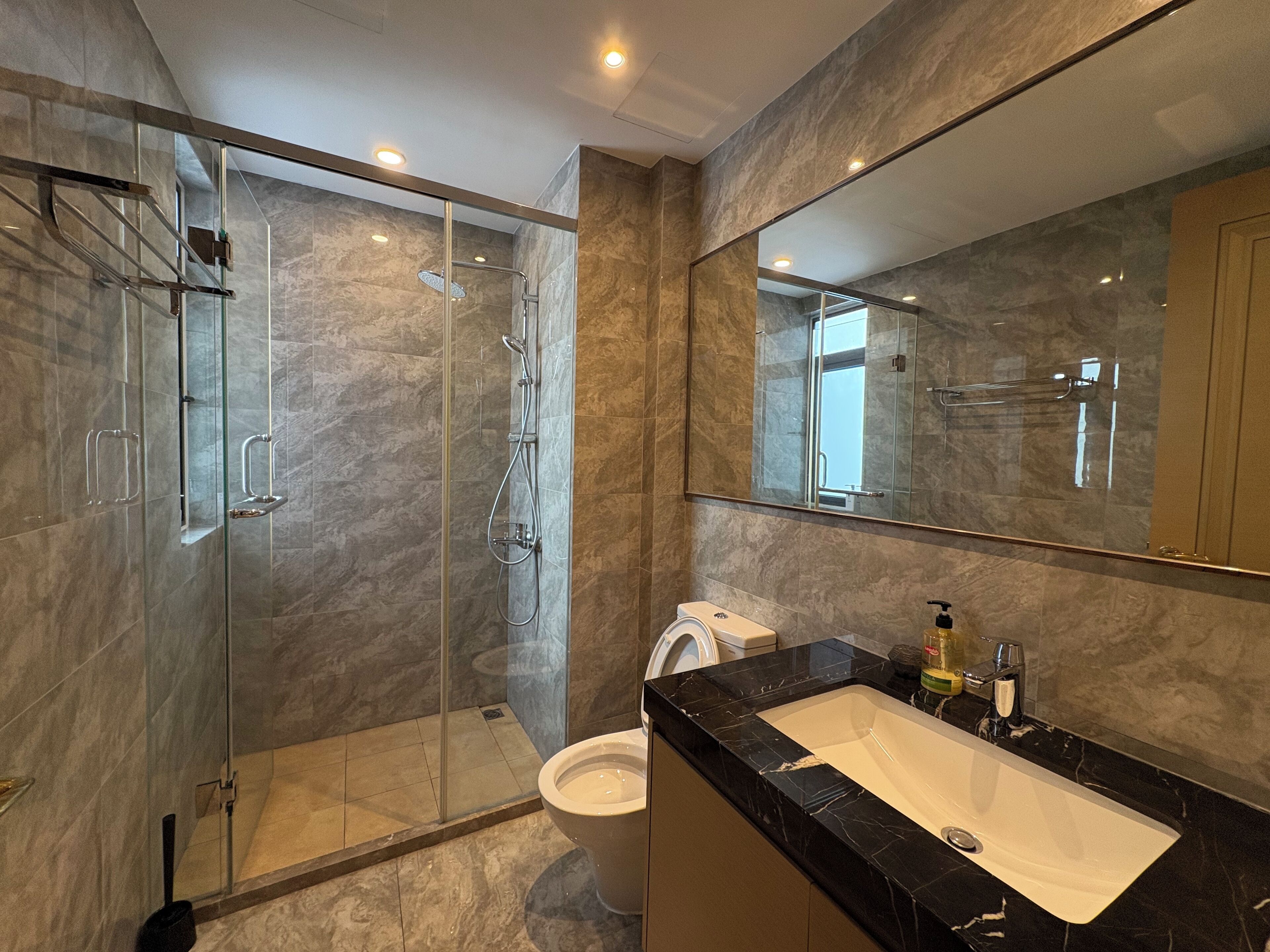 Ein modernes Badezimmer mit einer gläsernen Dusche, einer weißen Toilette und einem schwarzen Marmorwaschbecken.