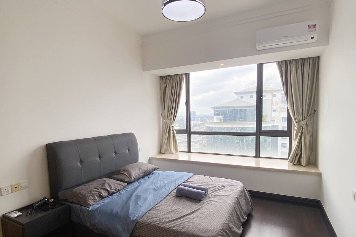 Une chambre à coucher avec un lit, une table de chevet, un climatiseur et une fenêtre avec des rideaux.