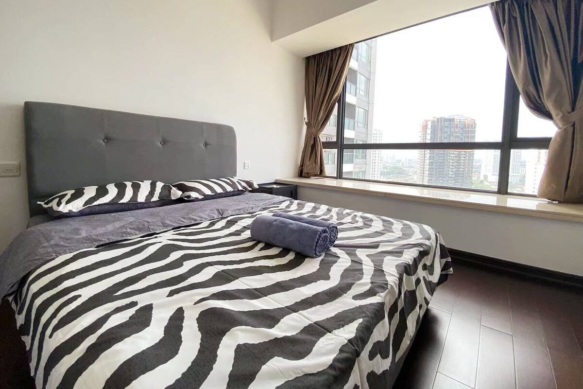 Une chambre avec un grand lit, une fenêtre avec des rideaux et une vue sur les bâtiments environnants.