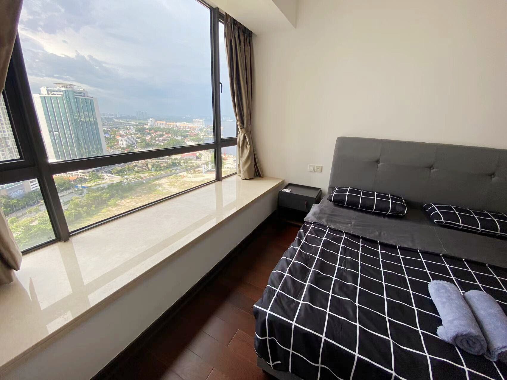 A bedroom with a large window, a bed with a black and white checkered bedspread, and a grey headboard.