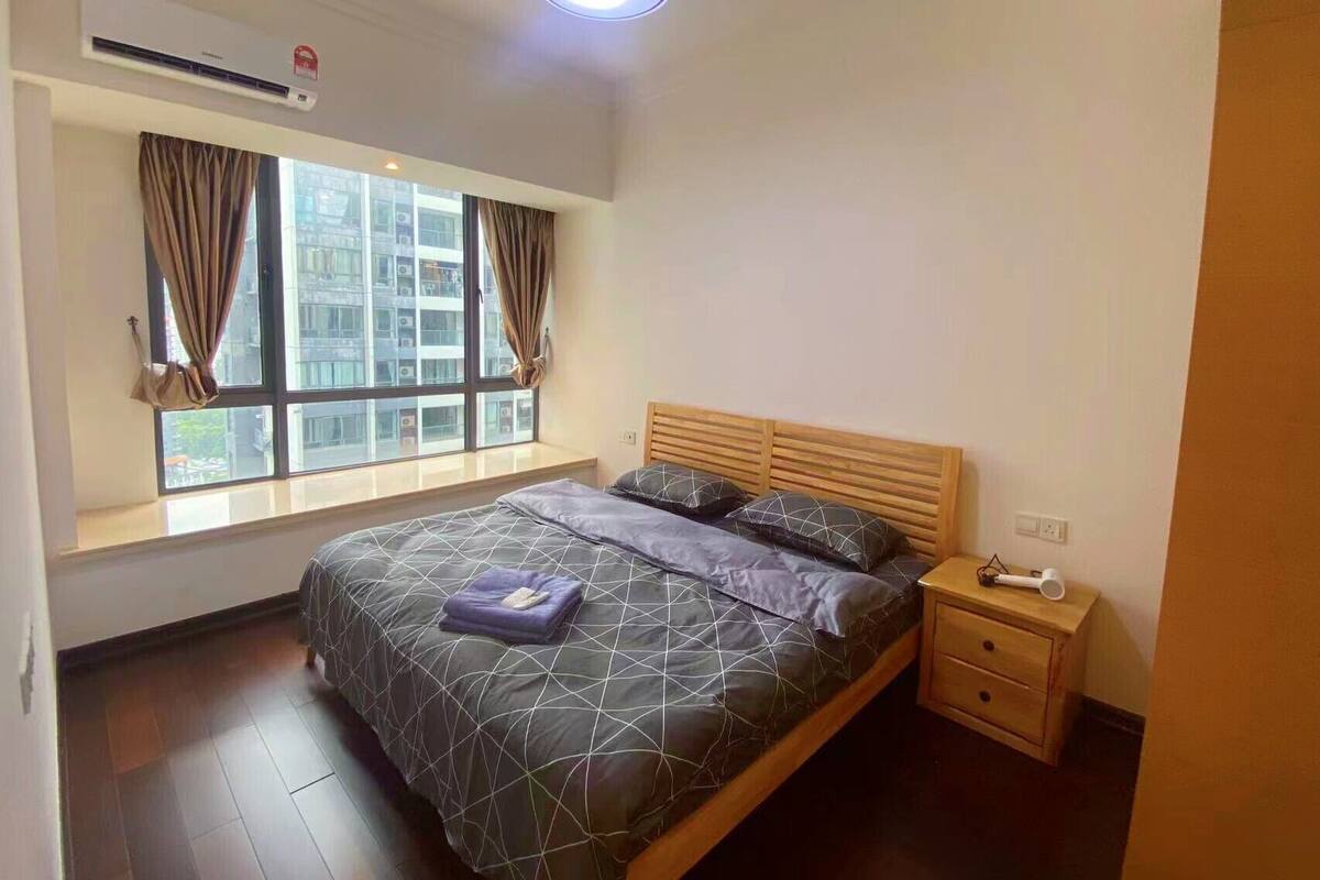 Une chambre à coucher avec un lit, une fenêtre avec des rideaux, une table de chevet et un appareil de climatisation.