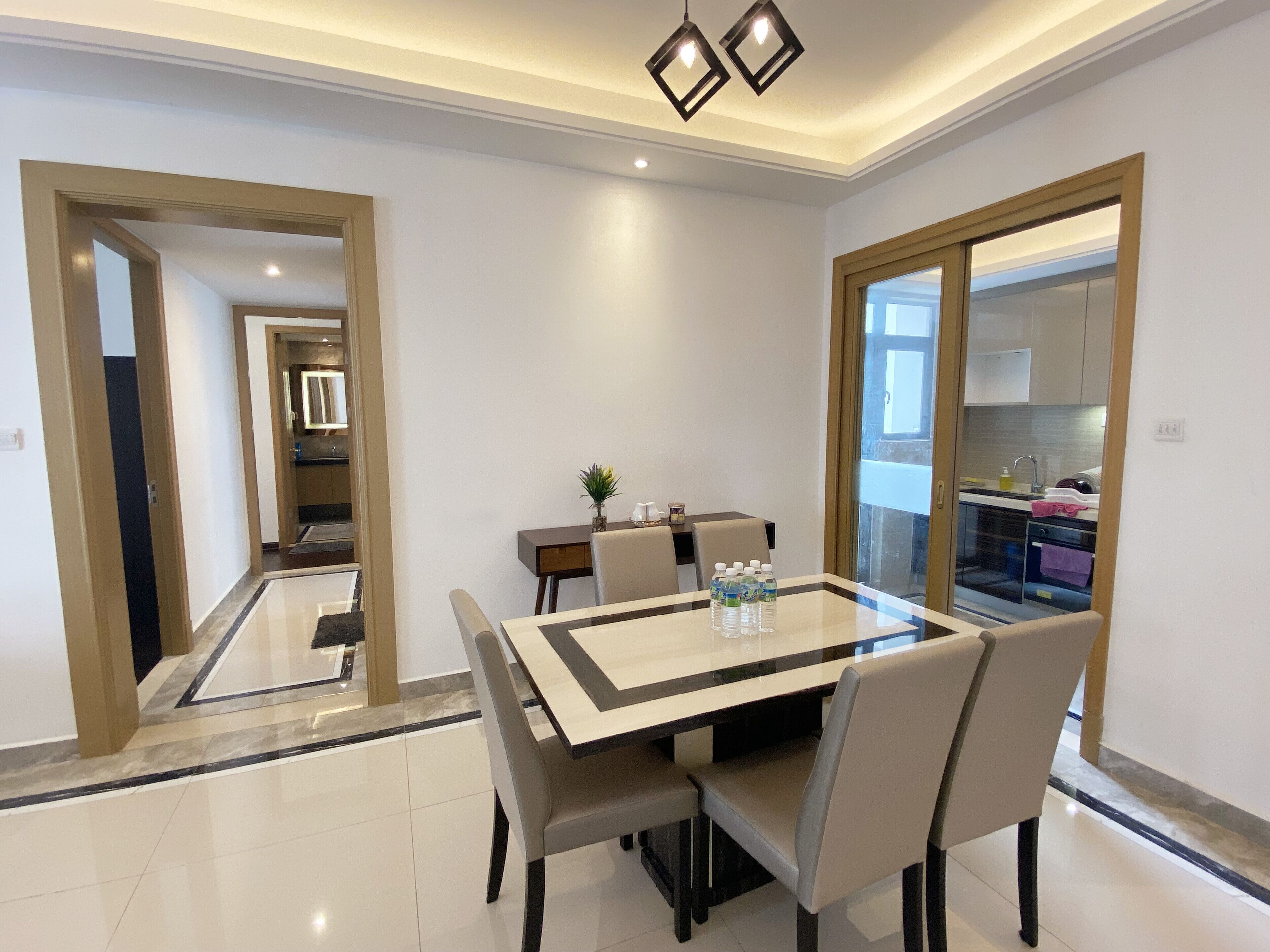 A modern dining area with a glass table, four chairs, and a small side table with a plant and water bottles.