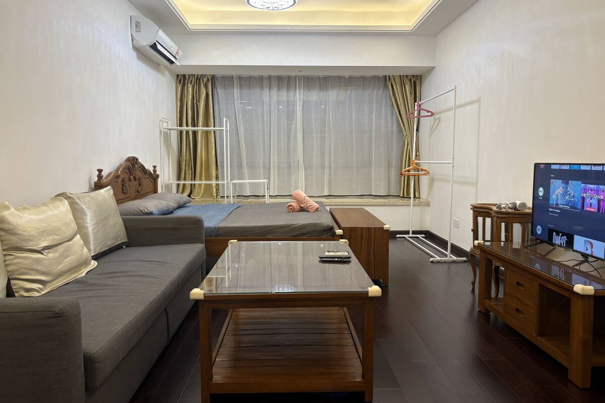 Un salon moderne avec un canapé, une table basse en bois, un téléviseur et une fenêtre avec des rideaux.